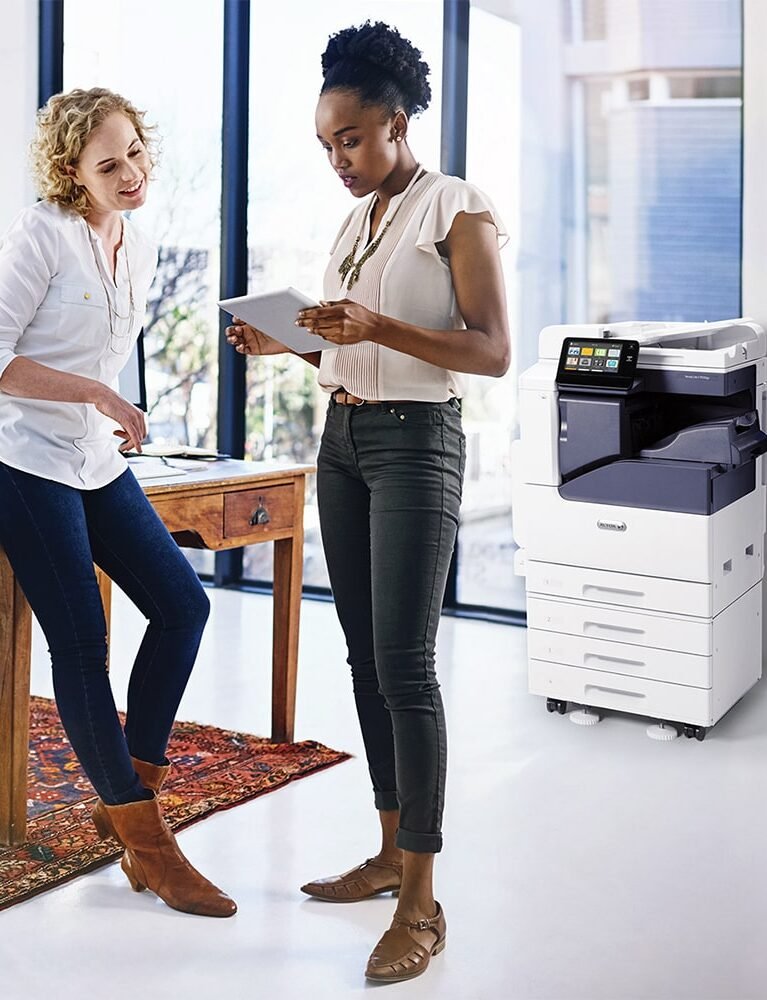 Two people looking at a tablet screen with a photocopier in the background